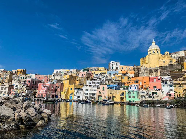 Marina di Corricella in Procida dozens of pastel colored houses that make up a fishing village on the island of Procia seen from the boat